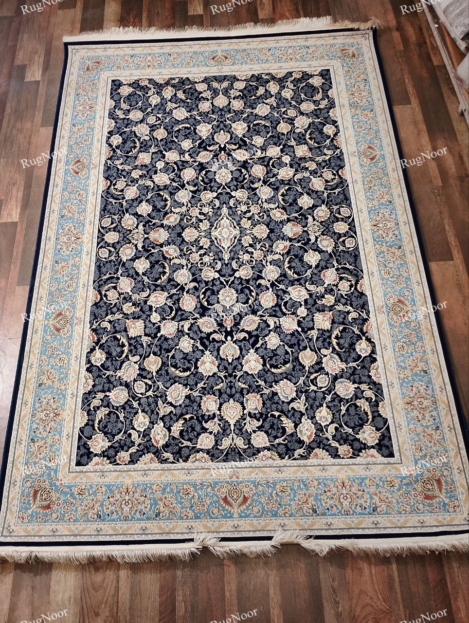 Full view of the Lajvard navy blue floral rug featuring an all-over ivory and blush floral pattern, a light blue and ivory ornamental border, and cream fringe on a wooden floor.