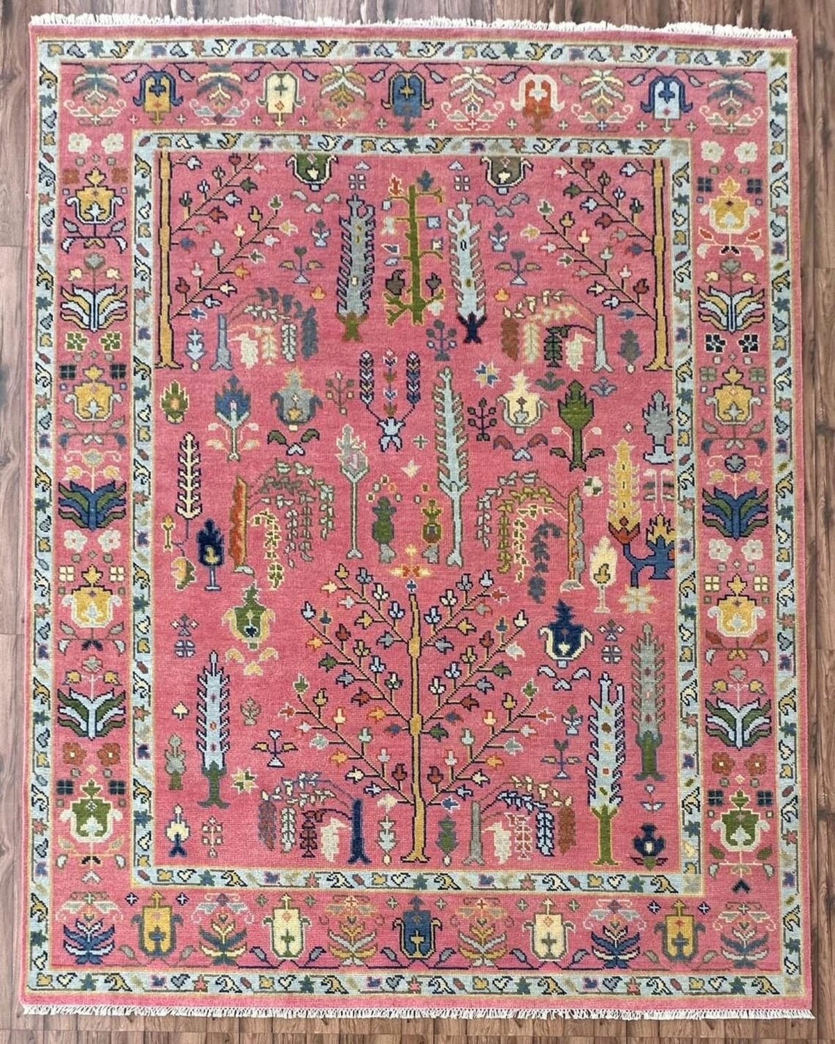 Alcazar Palace hand-knotted Oushak wool rug in dusty rose with a central flowering tree, colorful botanical motifs, and an intricate ivory border