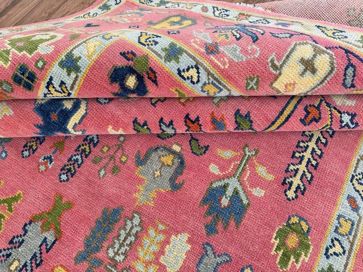 Close-up of Alcazar Palace Oushak wool rug showing the hand-knotted pile, dusty rose field, and multicolor botanical motifs