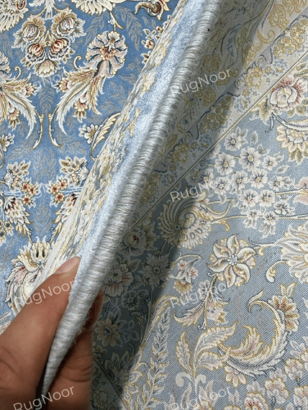 Nardine carpet folded back to show its dusty blue floral surface, pale underside, and thick finished edge.