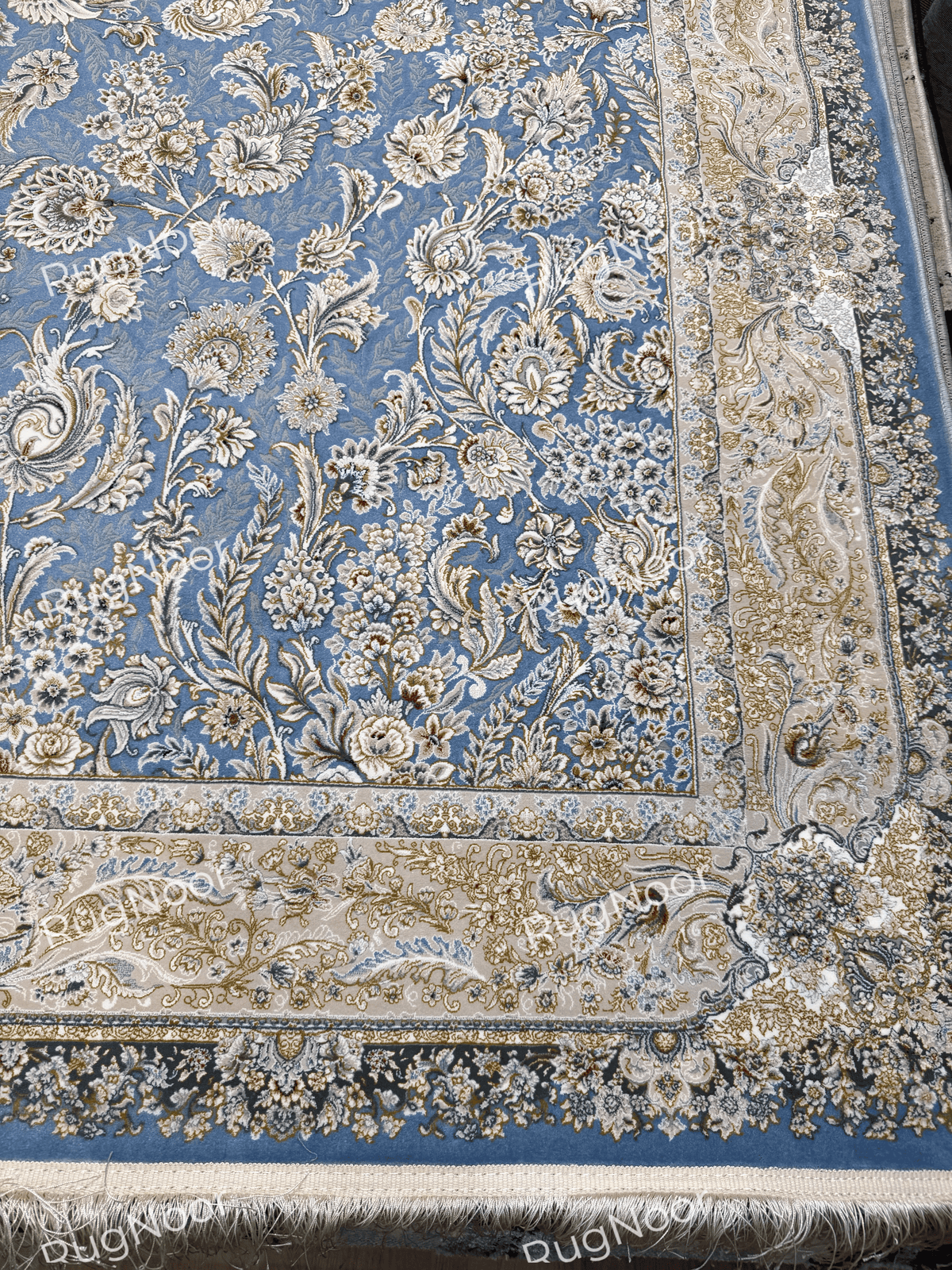Nardine carpet showing the floral border, dusty blue field, and ivory fringe along the edge.
