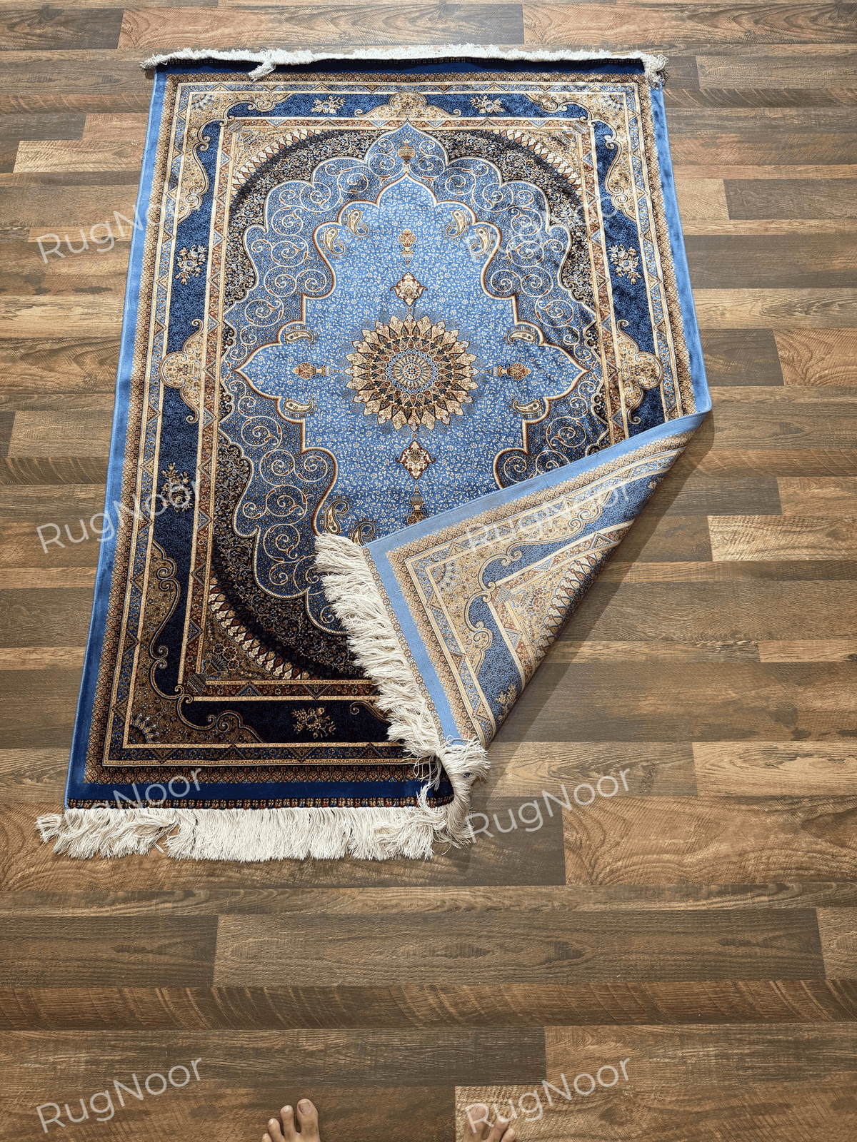 Yasamin folded corner showing the patterned underside, blue edging, and ivory fringe.