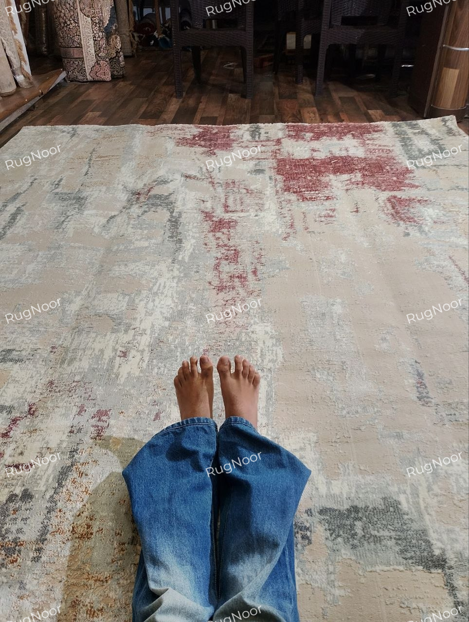Person sitting on the Amselle modern abstract rug, showing its muted colours and appearance in a living space.