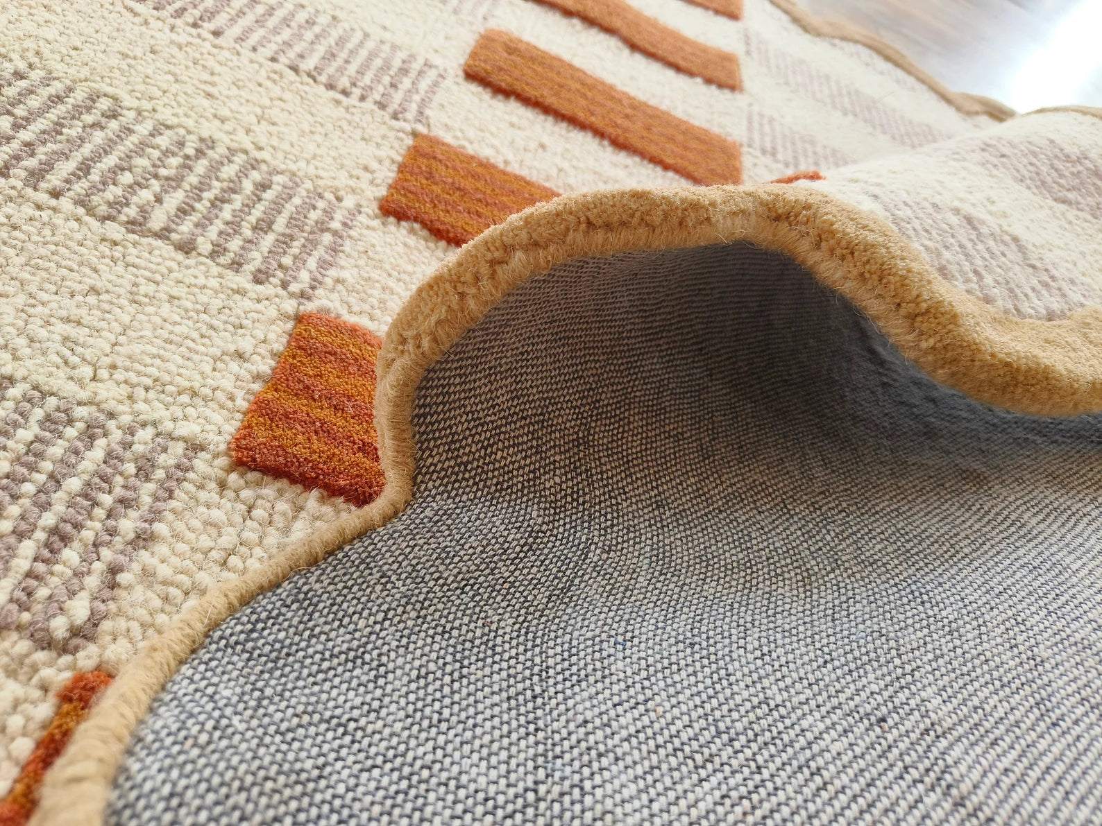 Close-up of a woven area rug showing the top patterned surface and the underside in a heather gray fabric, with a folded edge revealing the texture.