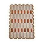 A rectangular area rug with a scalloped jute border, featuring a checkered pattern of beige, taupe, and rust-orange squares on a white background.
