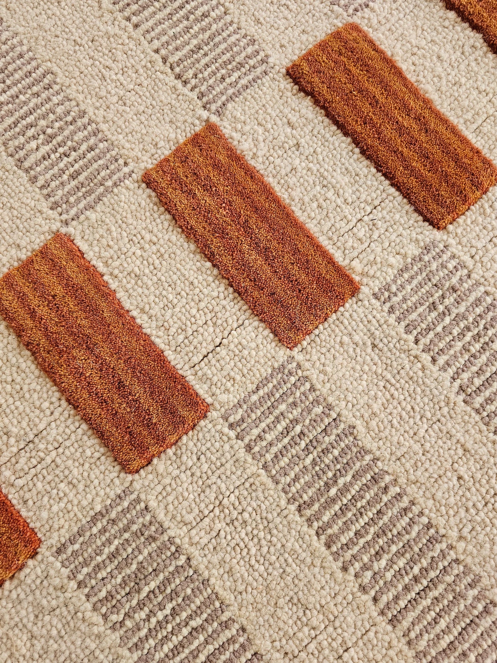 Close-up of a textured area rug with a geometric pattern featuring rust-orange rectangular blocks and taupe-beige striped blocks on a cream background.