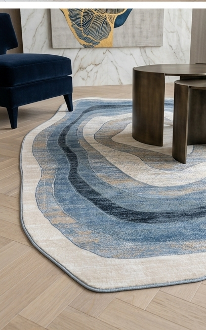 An abstract wavy area rug in shades of blue, gray, and beige, styled in a modern living room setting with a dark blue armchair, round wooden coffee tables, and a marble wall.