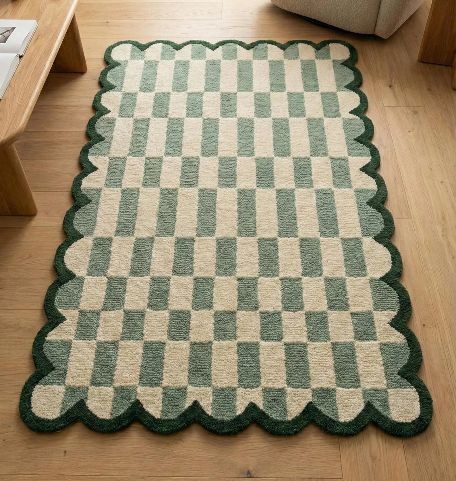 A rectangular area rug with a scalloped edge, featuring a green and beige checkerboard pattern, shown on a light wood floor.