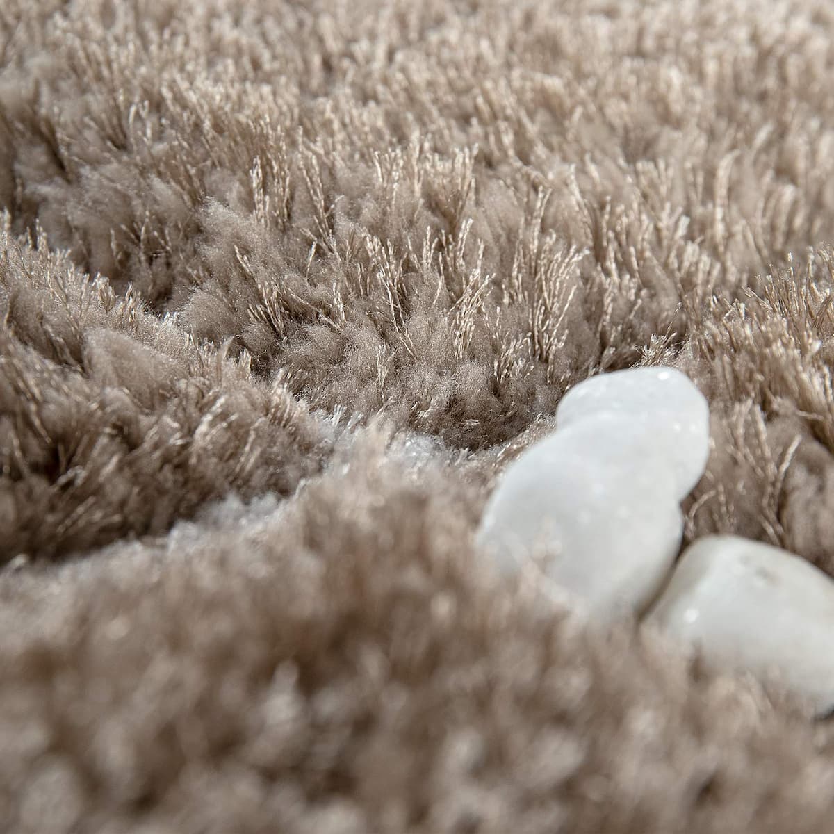 Close-up of a plush, shaggy rug in a warm taupe-beige color, with two smooth white stones placed on the surface.