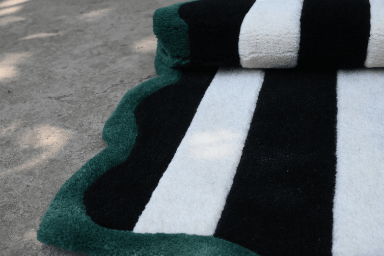 Close-up of a black, white, and green striped rug on a concrete floor.