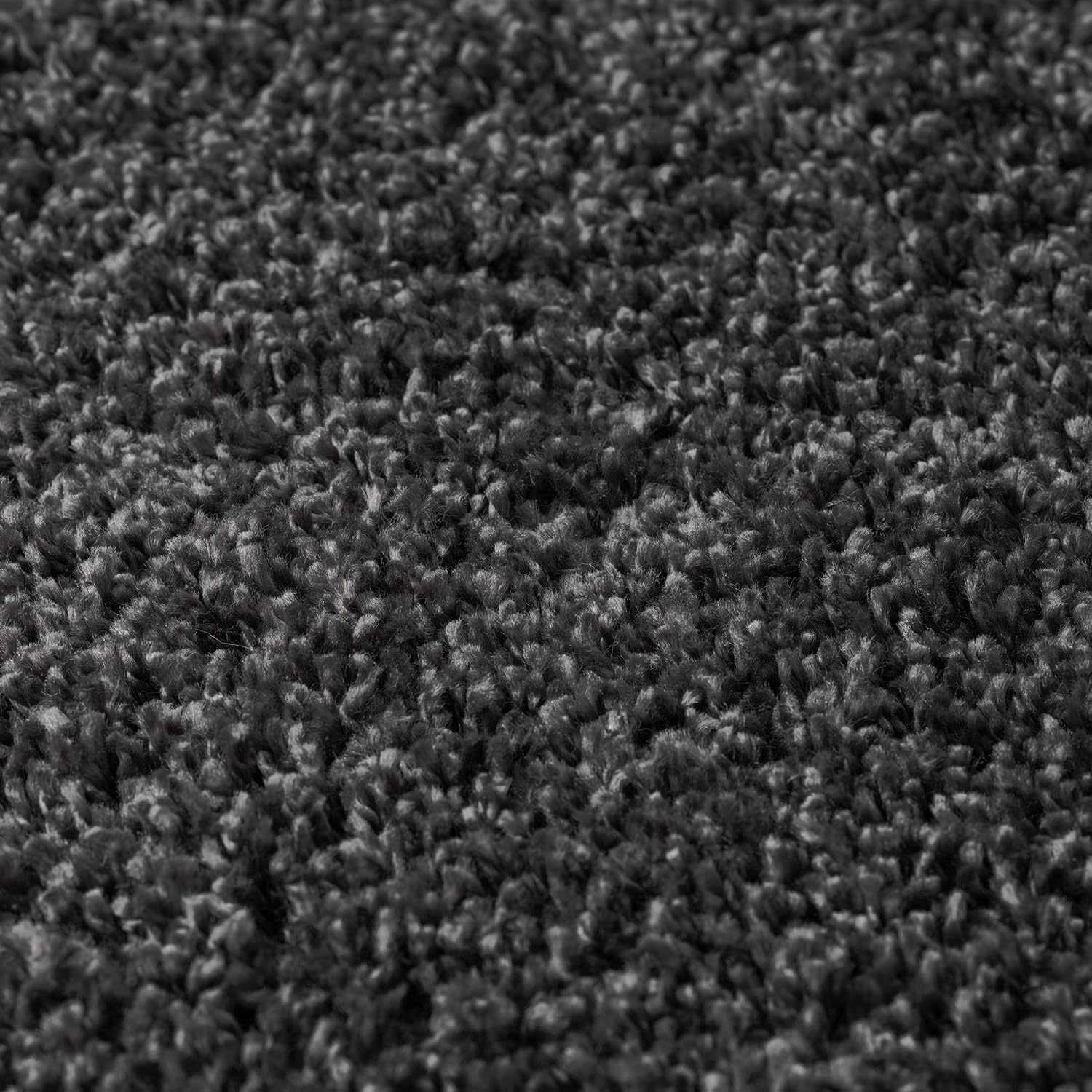 A close-up texture shot of a dark charcoal gray loop pile carpet, showing the dense, high-pile fibers in detail.