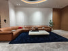 Modern living room with a brown sectional sofa, white coffee table, and dark blue rug.