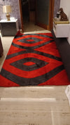 Red and black patterned rug on a wooden floor with a lamp and cabinet in the background.