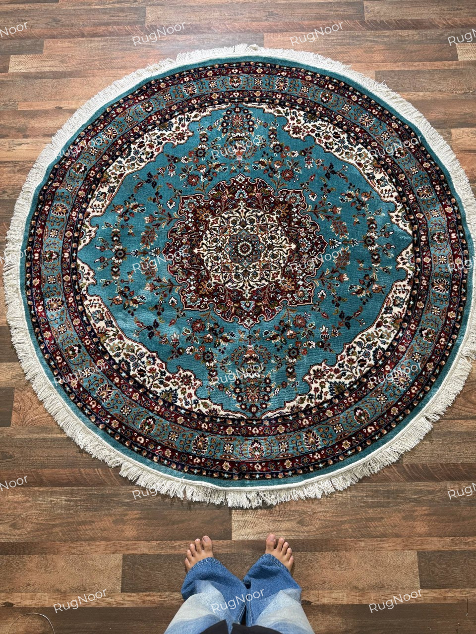 Fayruz round turquoise rug featuring dense floral motifs, an ornate ivory medallion, burgundy borders and cream fringe - RugNoor