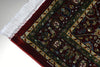 Corner detail of Firman Persian rug showing forest green border, deep crimson field and hand-finished ivory cotton fringe