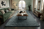 A large, soft rabbit fur carpet, area rug in a grey color, styled in a modern, elegant living room with a green sofa, wooden coffee table, and dark tiled floors.