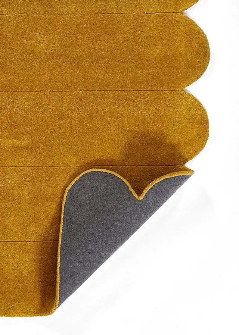 A close-up of a mustard yellow suede-like fabric product with scalloped edges, showing a folded underside with a dark gray backing on a white background.