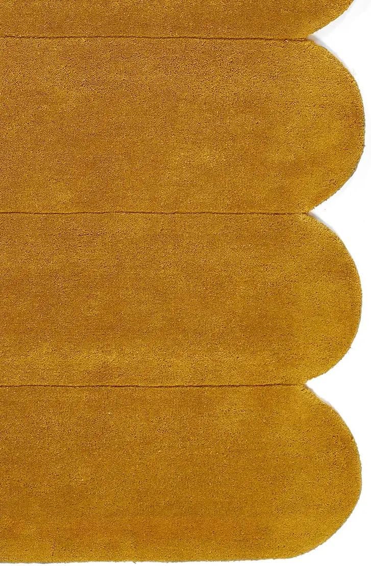 A close-up of a mustard yellow fabric or material swatch with a scalloped cut edge, shown against a white background.