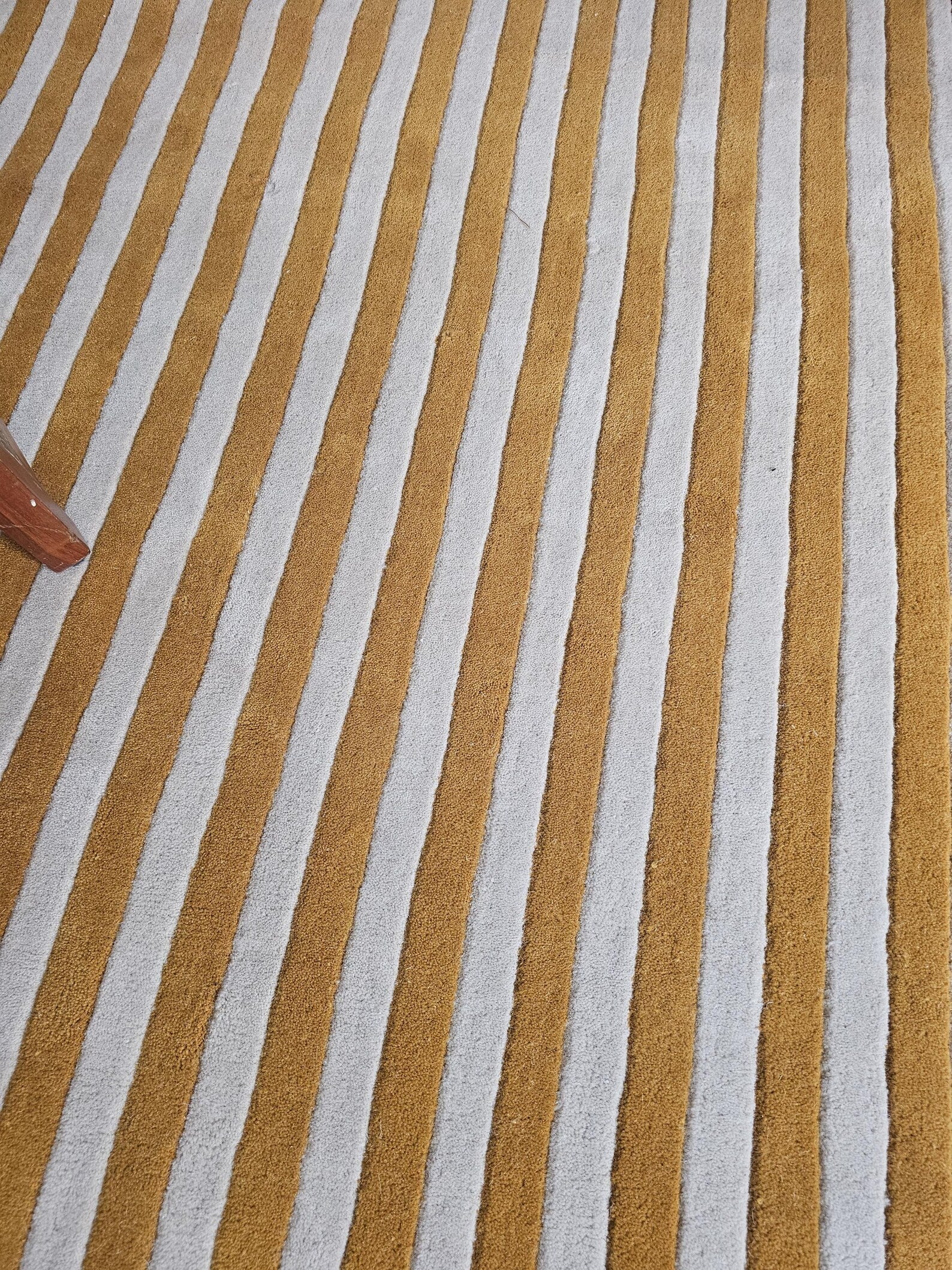 A close-up of a striped textile or rug with alternating warm mustard-gold and off-white vertical stripes.