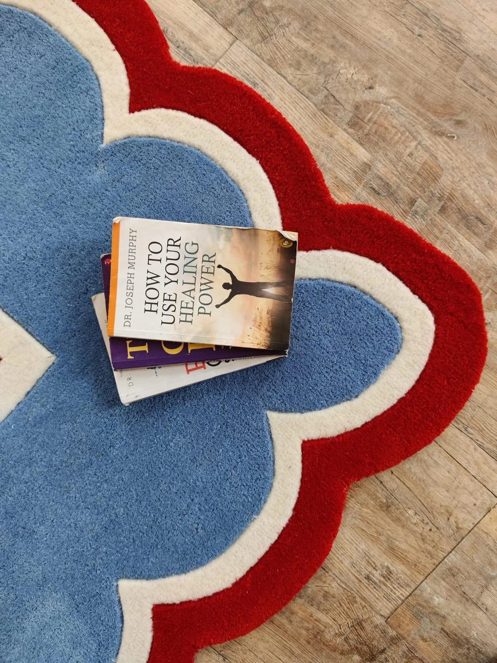 A stack of two books, with the top book titled 'How to Use Your Healing Power' by Dr. Christopher Matthews, placed on a blue, red, and white patterned rug over a light wood floor.