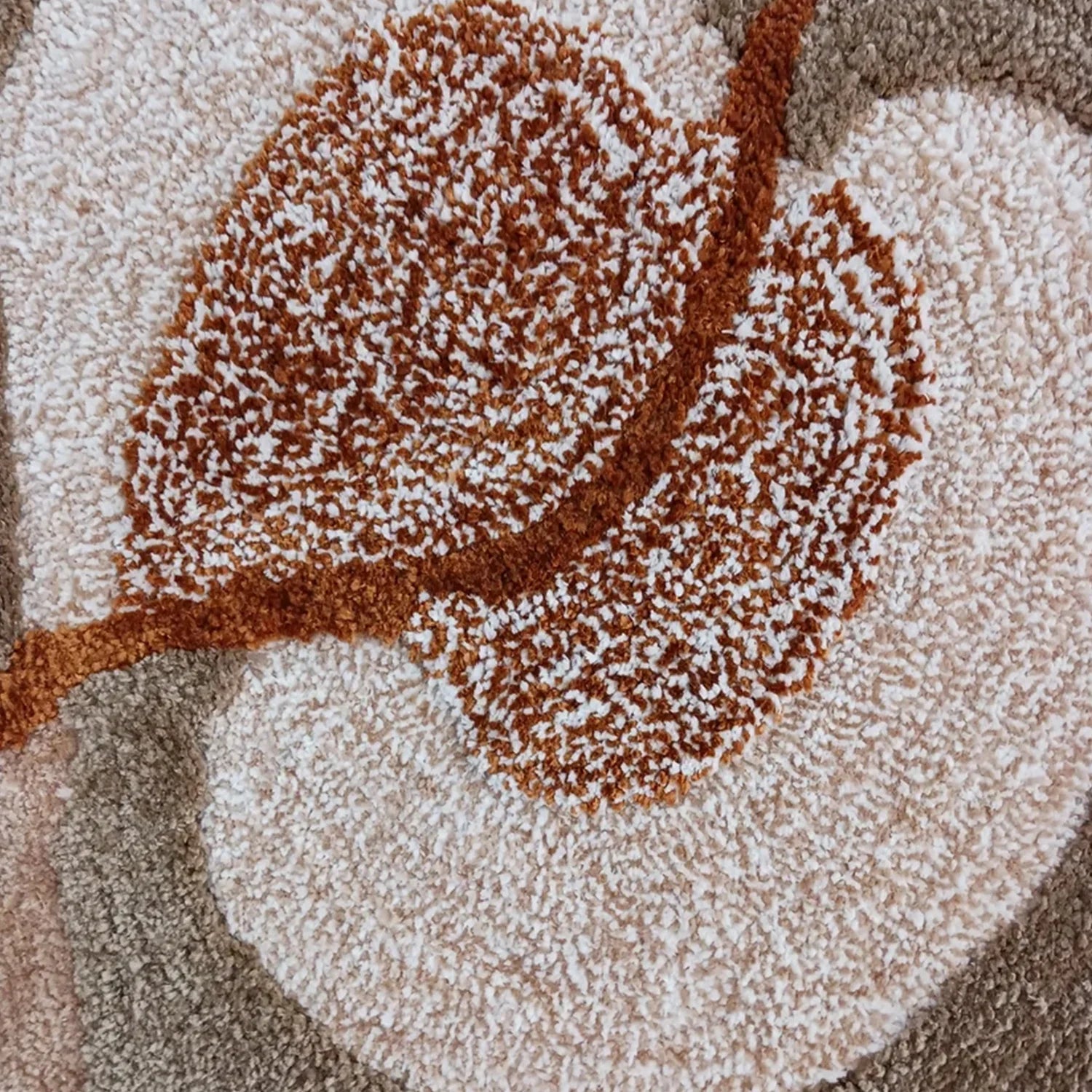 Close-up of a textured loop-pile rug featuring a large brown leaf motif over a warm beige and taupe background.