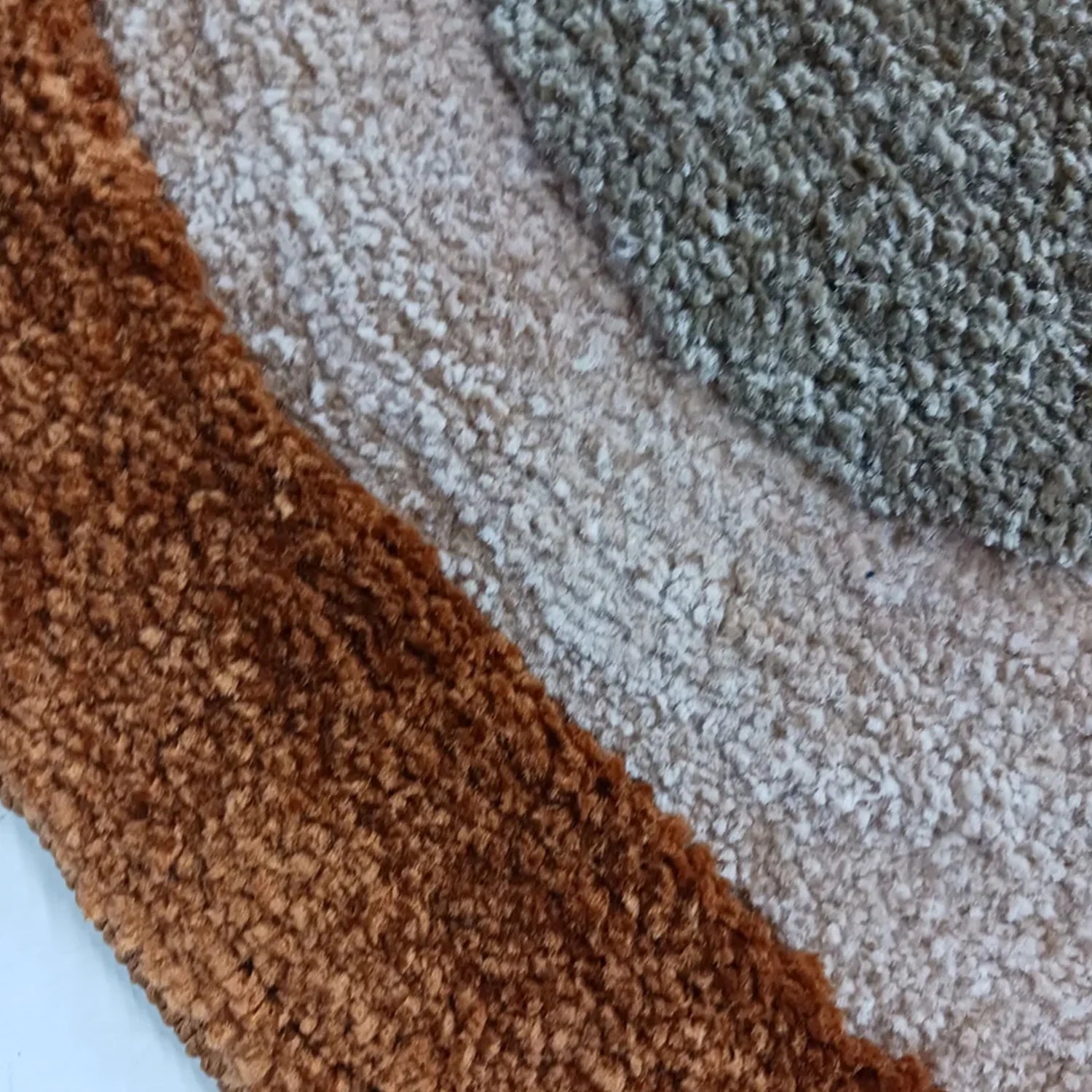 Close-up of a textured area rug with three curved color sections: a warm brown section, a light beige section, and a gray-green section.