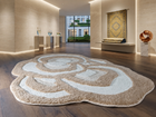 An abstract, organic-shaped shag rug in beige and off-white tones, displayed on a dark wood floor in a modern, upscale gallery or showroom.