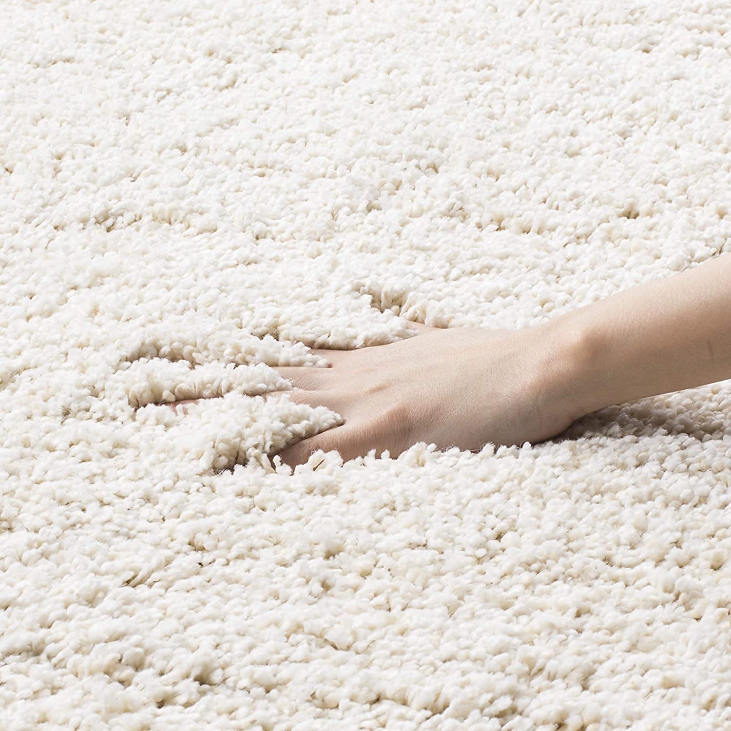 A close-up of a hand pressing into a thick, plush off-white shag carpet to show its texture and depth.