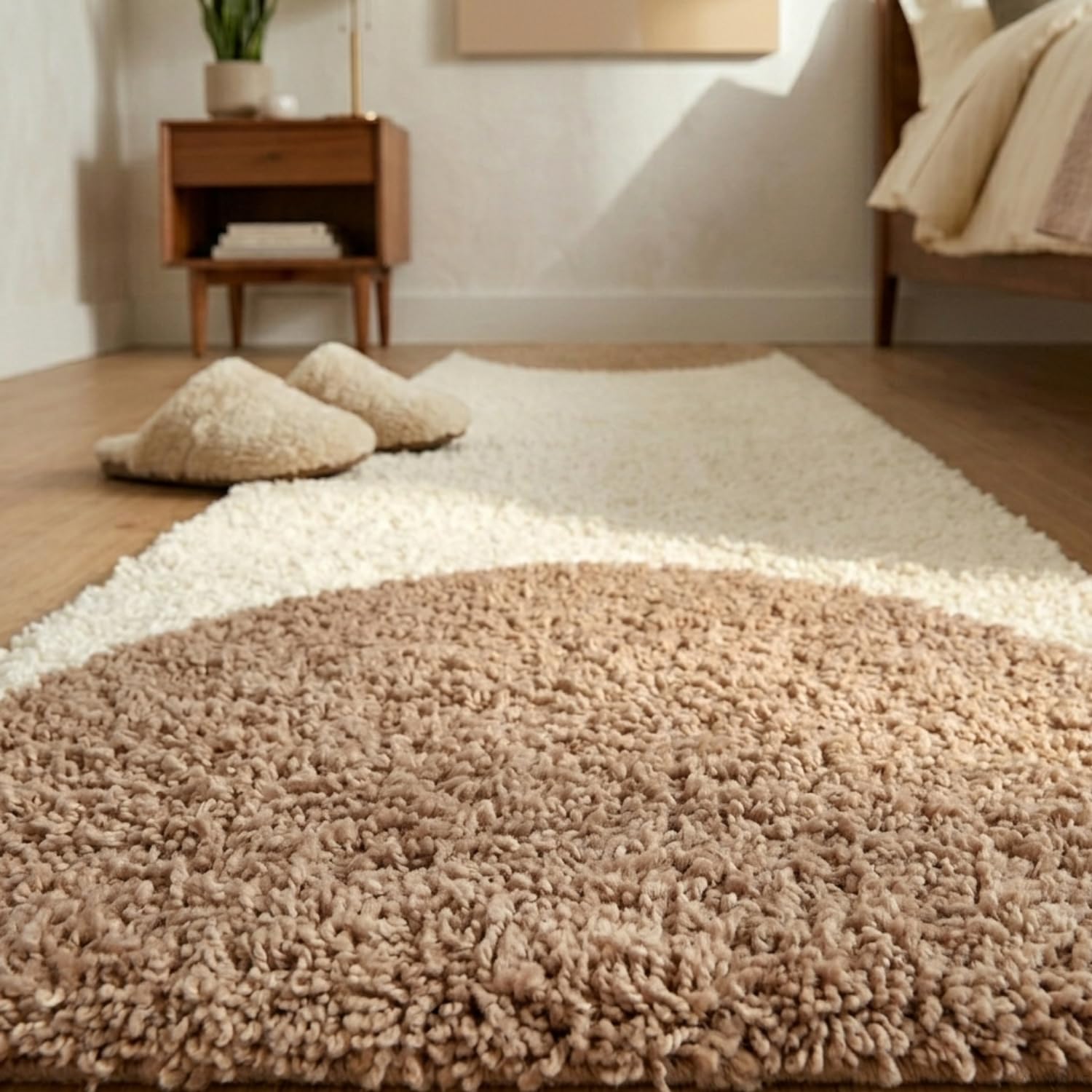 A round shag area rug in warm beige and cream, styled in a cozy bedroom setting with matching slippers on a wooden floor.