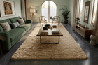 A large, textured beige area rug styled in a modern, elegant living room with a green sofa, wooden coffee table, and dark gray tiled floor.
