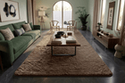 A large, plush, textured taupe beige area rug styled in a modern, elegant living room with a green sofa, wooden coffee table, and dark gray tiled floors.