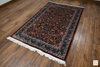 Naqsh Persian rug angled view on wood floor showing full pattern, teal border and cotton fringe