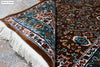 Corner fold of Naqsh Persian rug showing teal floral arabesque border, ivory cotton fringe and rug construction detail