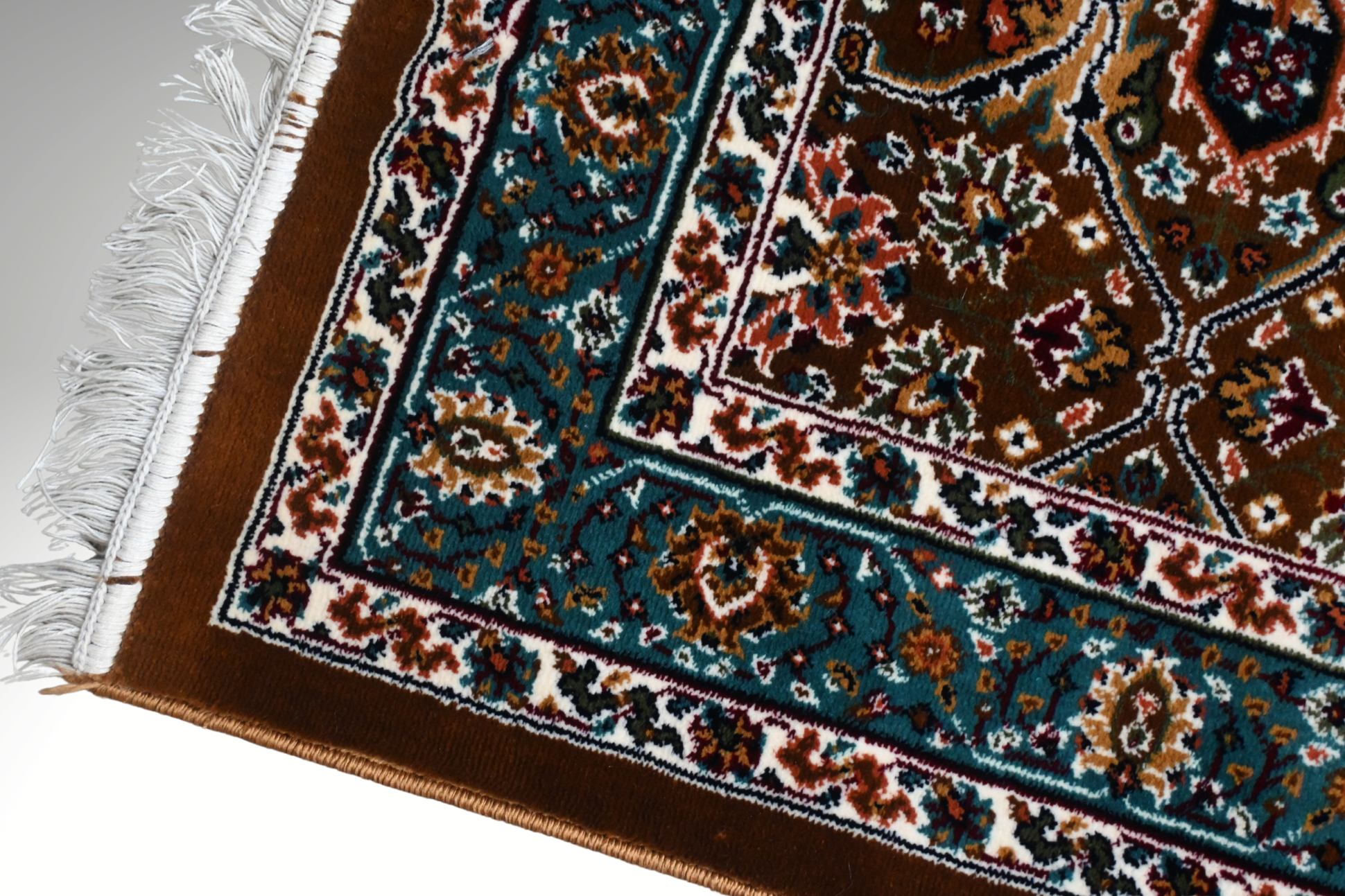 Corner detail of Naqsh Persian rug showing teal floral arabesque border, warm brown field and hand-finished cotton fringe