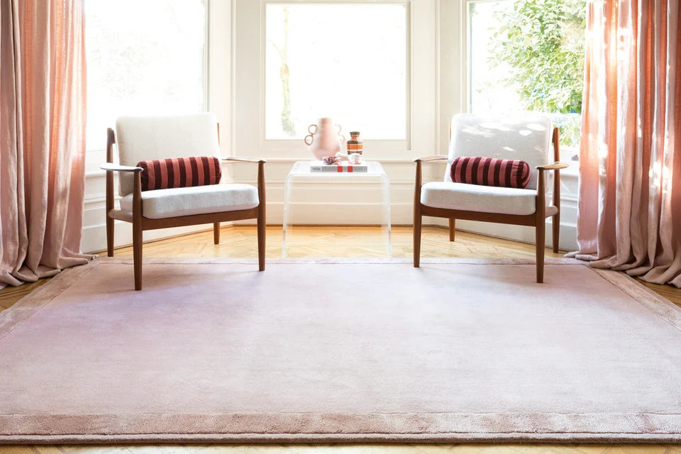 Pink border hand-tufted rug in sunlit living room with wooden armchairs