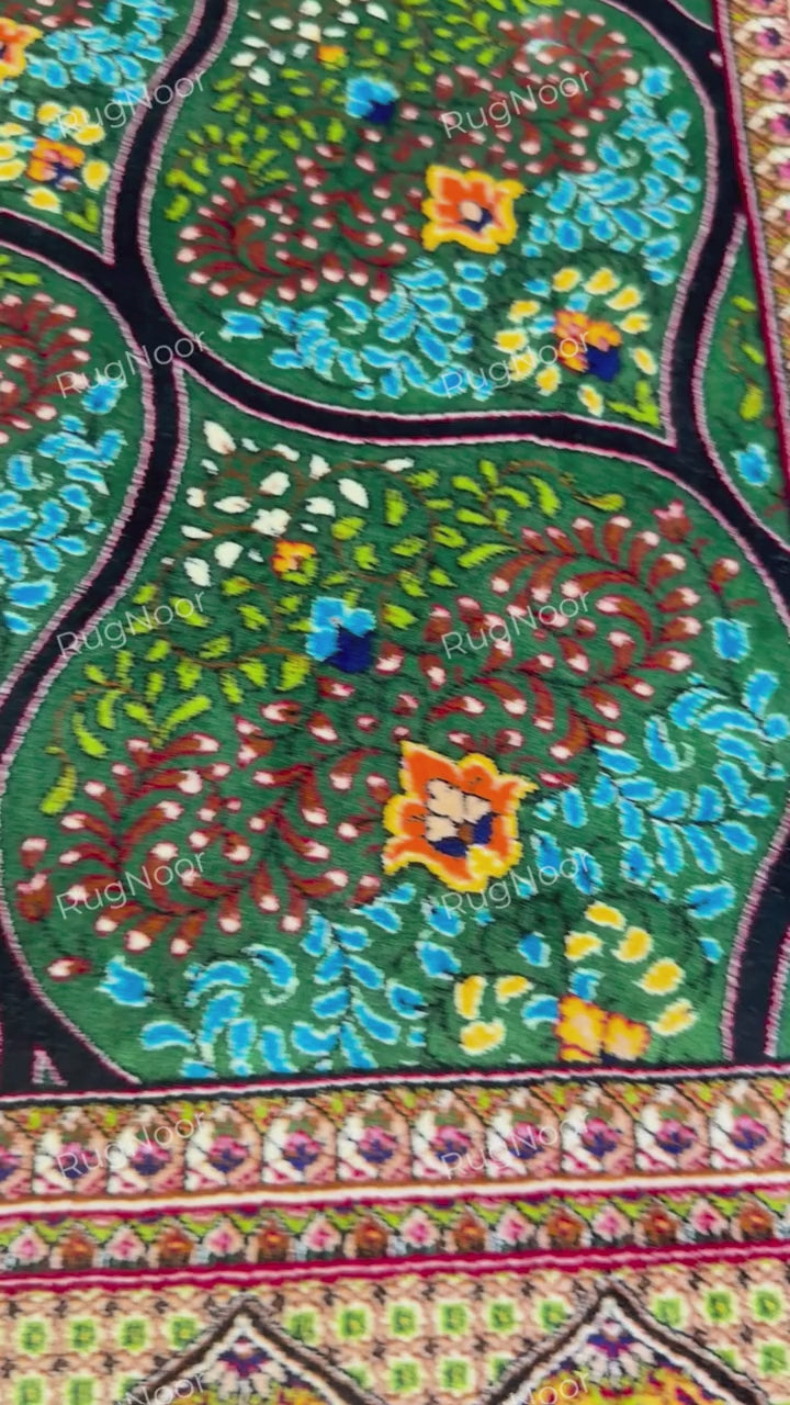 Detailed view of repeating teardrop-shaped motifs and colourful flowers across the green Tawus carpet and the border.