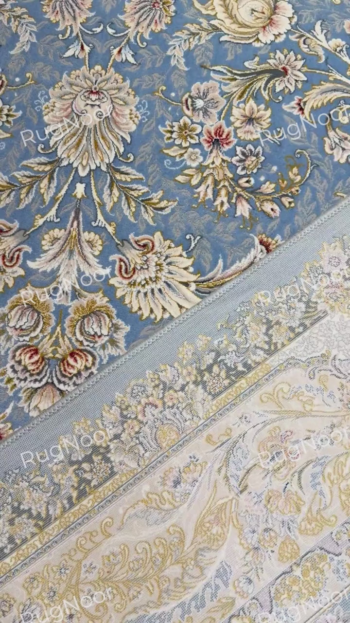 Nardine carpet folded back to show its dusty blue floral surface, pale underside, and thick finished edge.