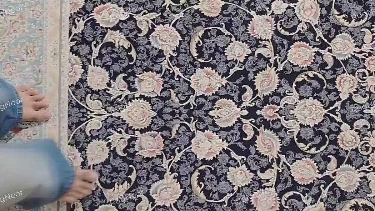 Top view of the Lajvard rug’s dense ivory, blush, and muted gold floral motifs linked by scrolling vines across a dark navy field, framed by a light blue and ivory border.