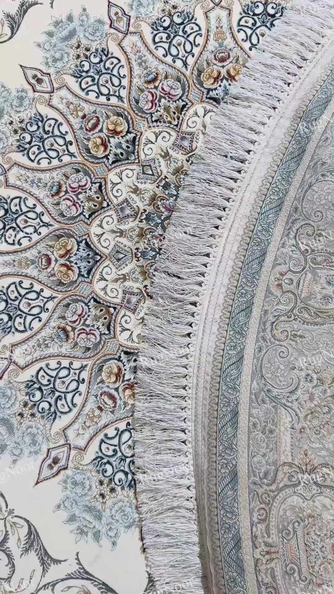 Close-up of the Mahzarin carpet showing ivory fringe beside the intricate blue-grey and taupe border and the central ivory floral field.