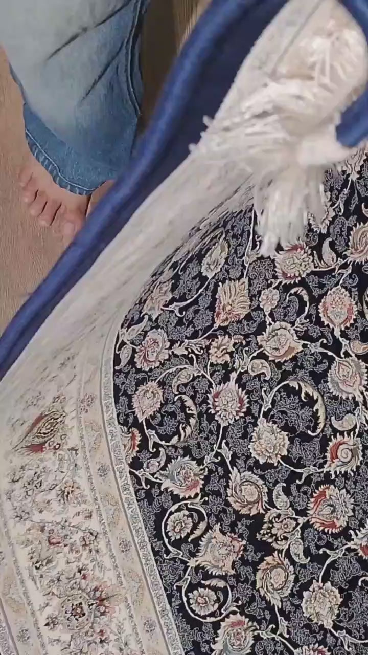 Folded corner of the Zarniva traditional carpet showing its brown underside, blue bound edge, ivory fringe and navy blue floral pattern.