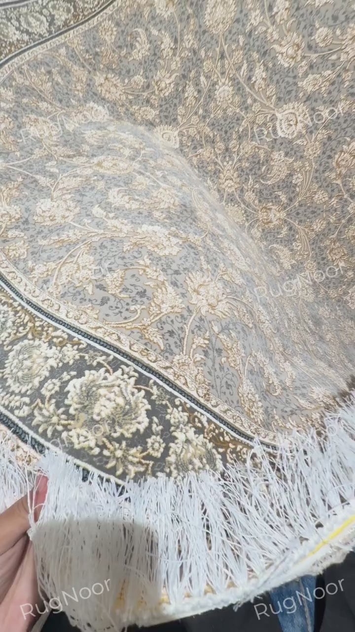 Close-up of the Golnaré carpet's curved grey surface with raised ivory and gold floral motifs and fine decorative outlines.