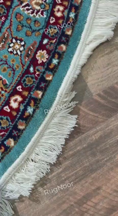 Folded corner of Fayruz round traditional rug showing the patterned underside, turquoise surface and ivory fringe - RugNoor