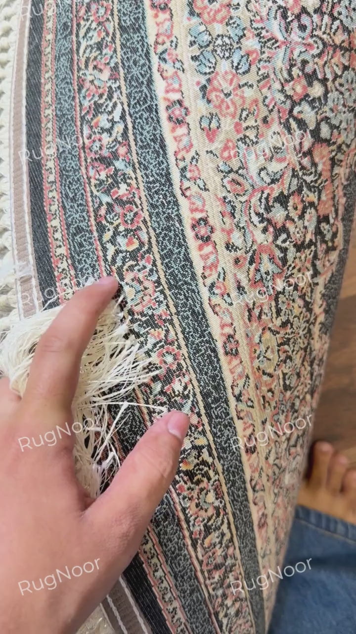 Close-up of the Ravzaran round carpet showing ivory fringe, a black ornamental band, and intricate rust, ivory, and blue floral detailing.