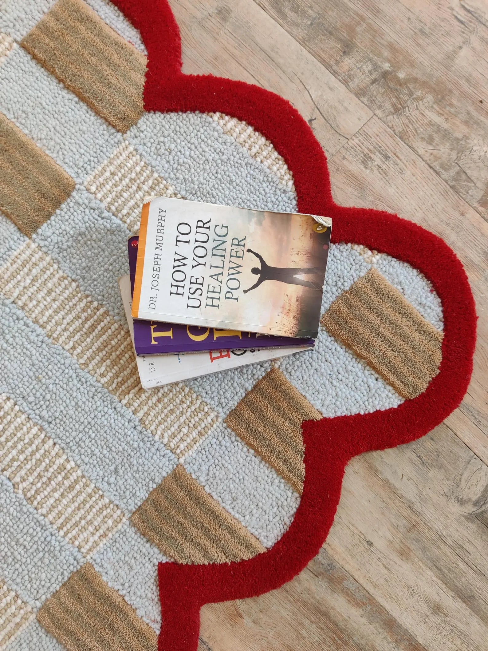 A stack of two books, including 'How to Use Forgiveness for Healing Power' by Dr. Joseph Murphy, placed on a heart-shaped area rug with a red border over a beige and gray checkered pattern, set on a light wood floor.