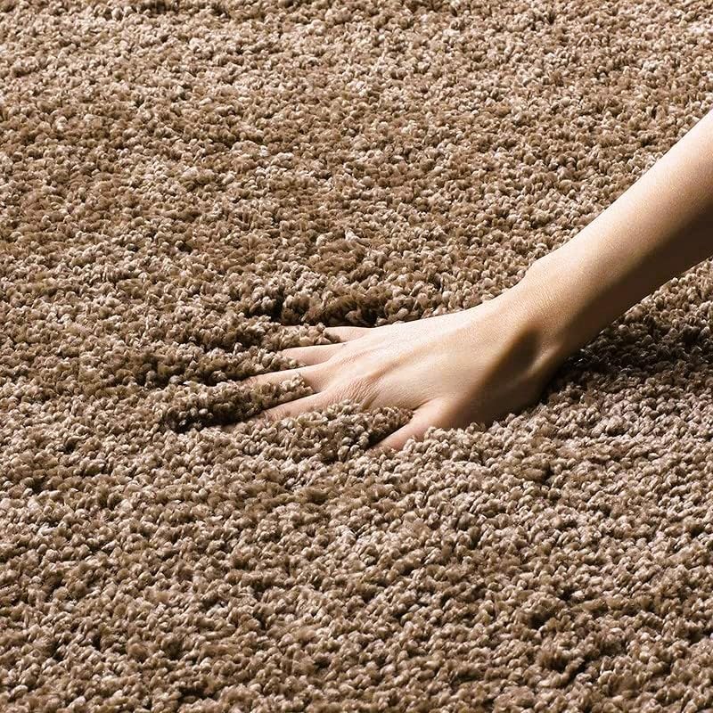 A close-up of a person's hand pressing down into a thick, high-pile brown carpet to show its texture and depth.