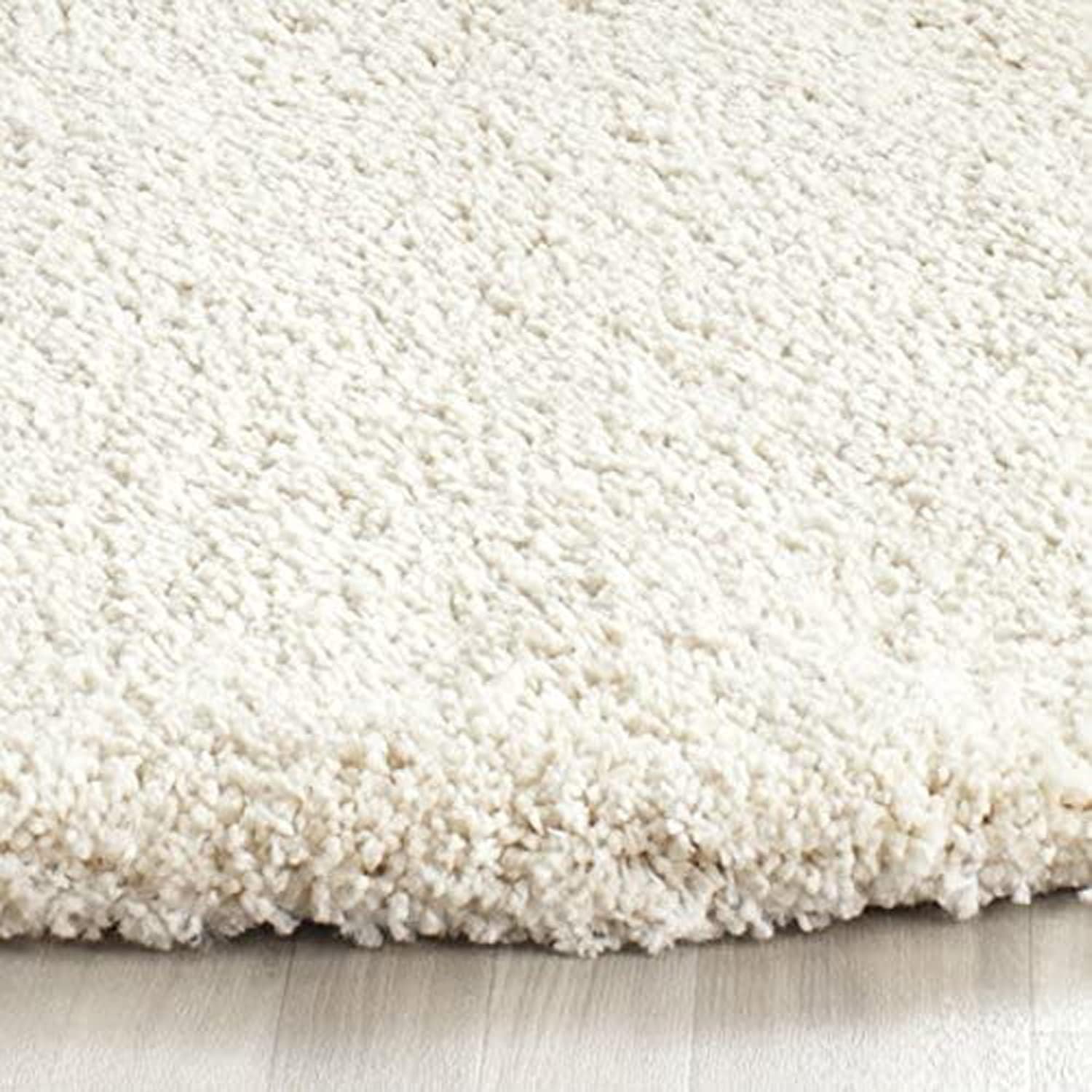 A close-up of a thick, plush shag rug in cream or off-white, showing its high-pile texture and the folded edge of the pile resting on a light wood floor.