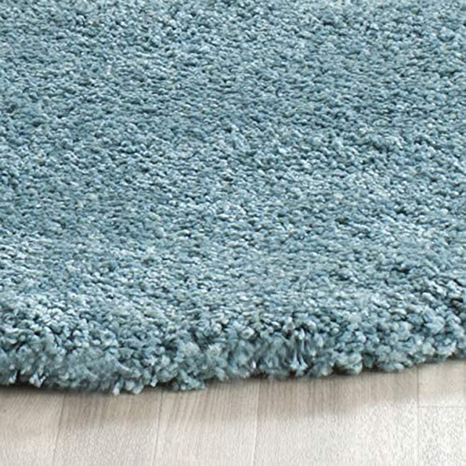 A close-up of a light blue shag rug with a thick, plush texture, shown resting on a light-colored wooden floor.