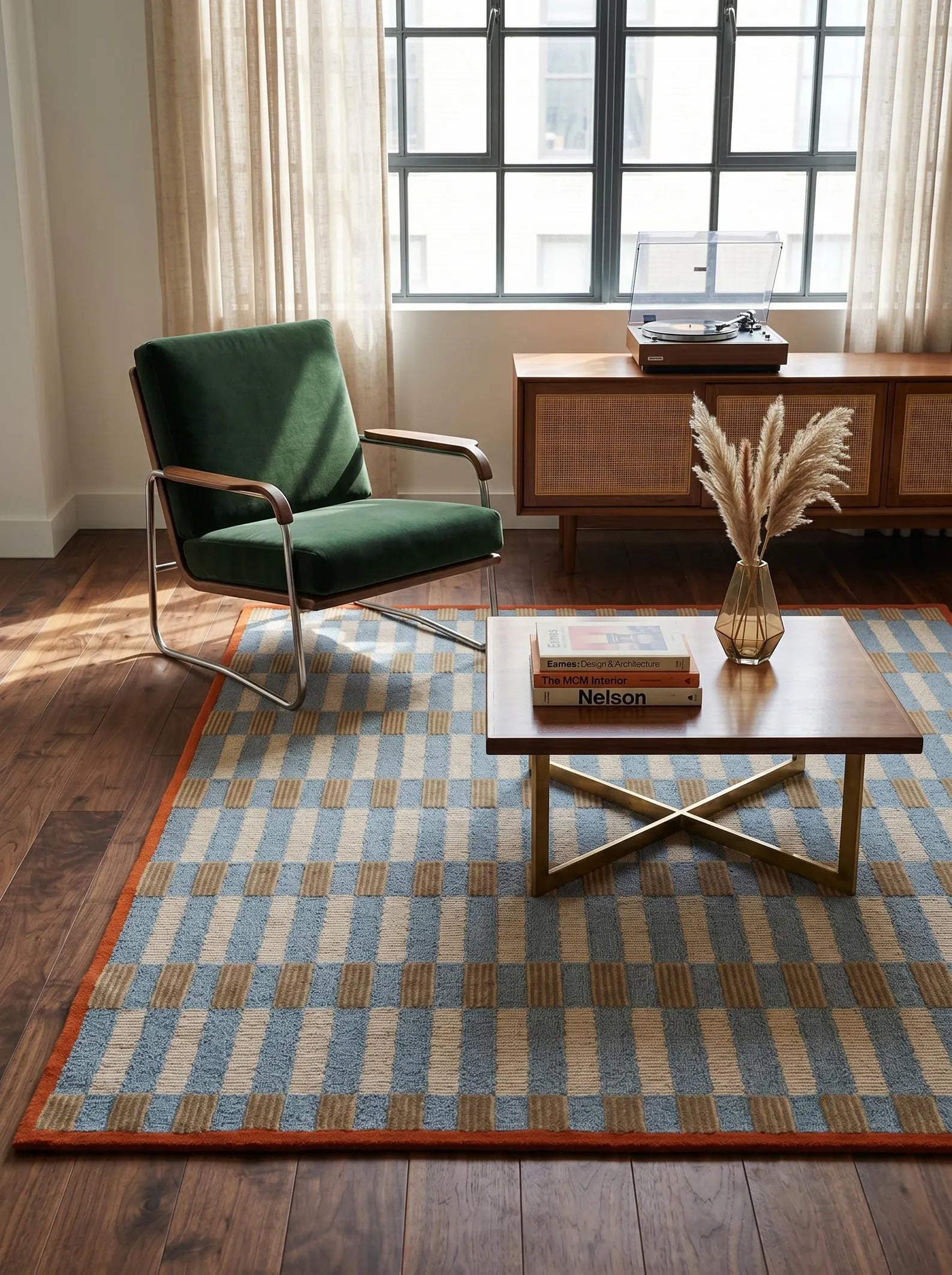 A styled living room scene featuring a blue, beige, and brown checkered area rug on dark wood floors, with a green armchair, a wooden coffee table, and a window in the background.