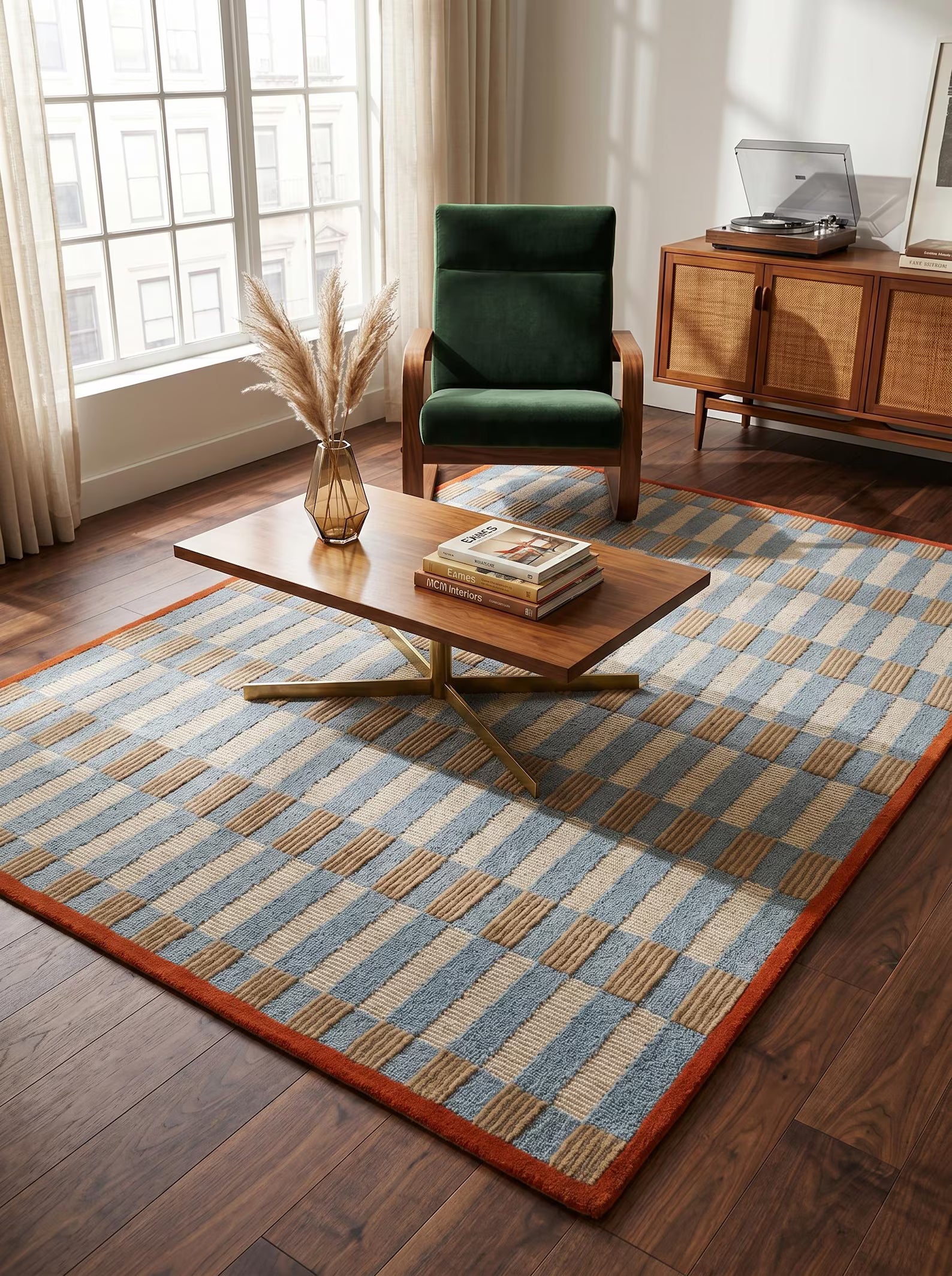 A large rectangular area rug with a blue, beige, and brown geometric basketweave pattern and a rust-orange border, styled in a bright modern living room with a wooden coffee table, green armchair, and wood credenza.