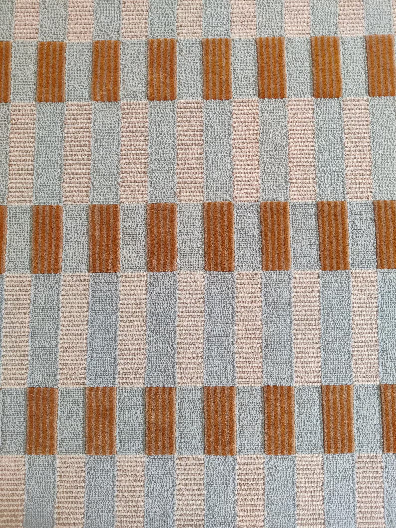 A close-up of a textured woven fabric with a geometric pattern of vertical stripes in light blue-gray, beige, and rust orange.